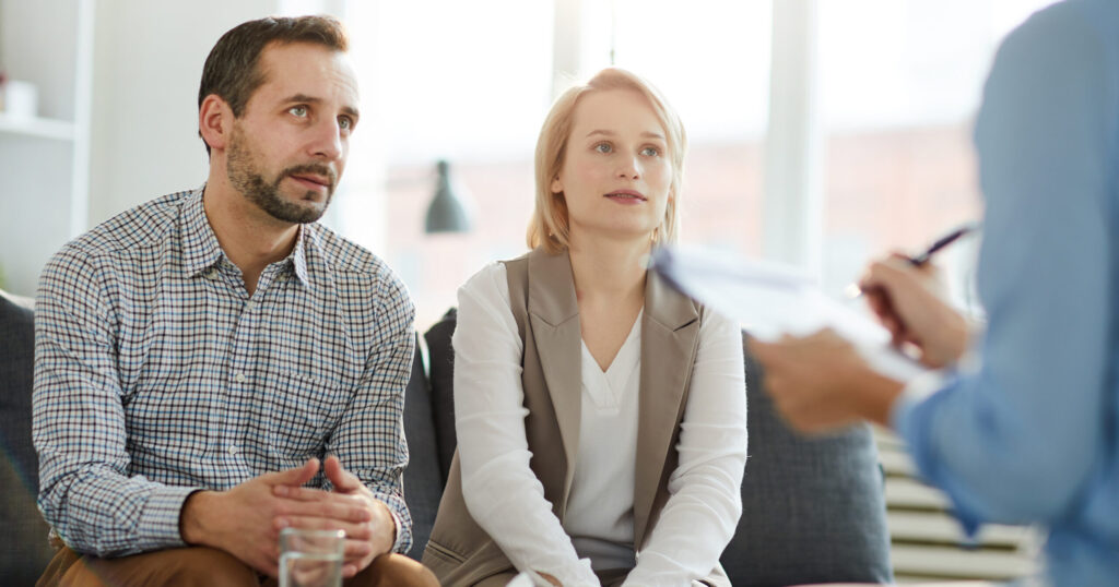Young couple sitting on couch in front of psychologist and listening to her advice at meeting