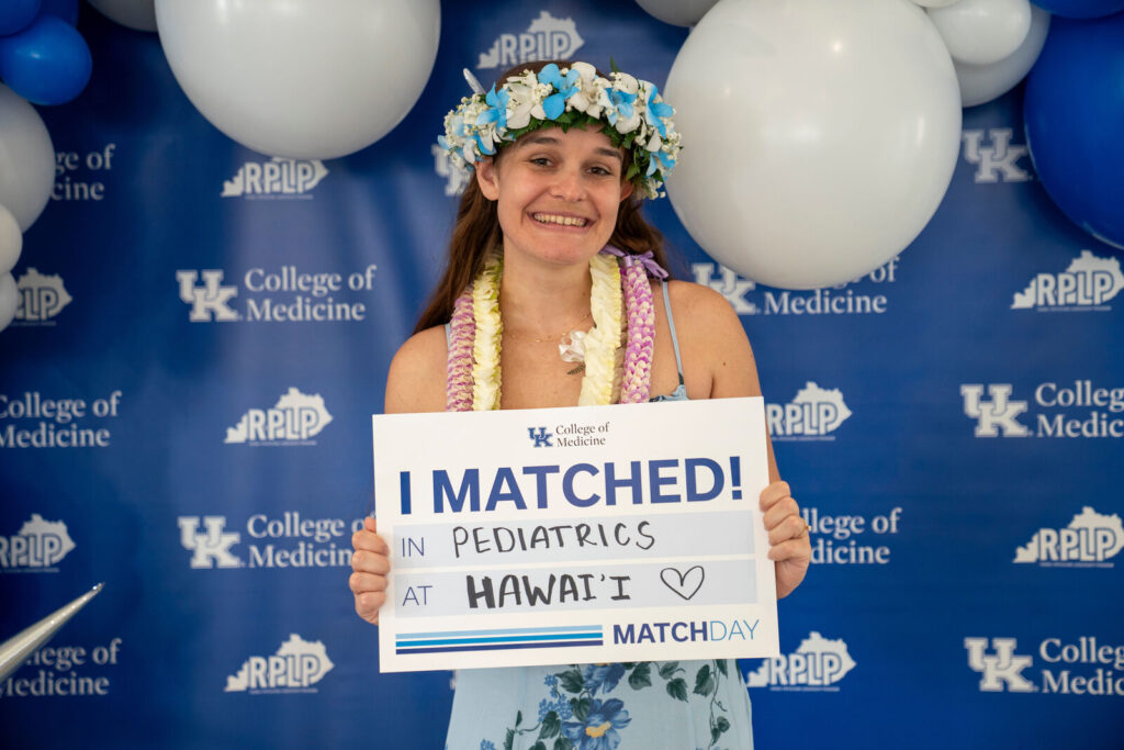 Madison Meister wears a flower crown and leis and holds an I Matched sign for Pediatrics at Hawaii.