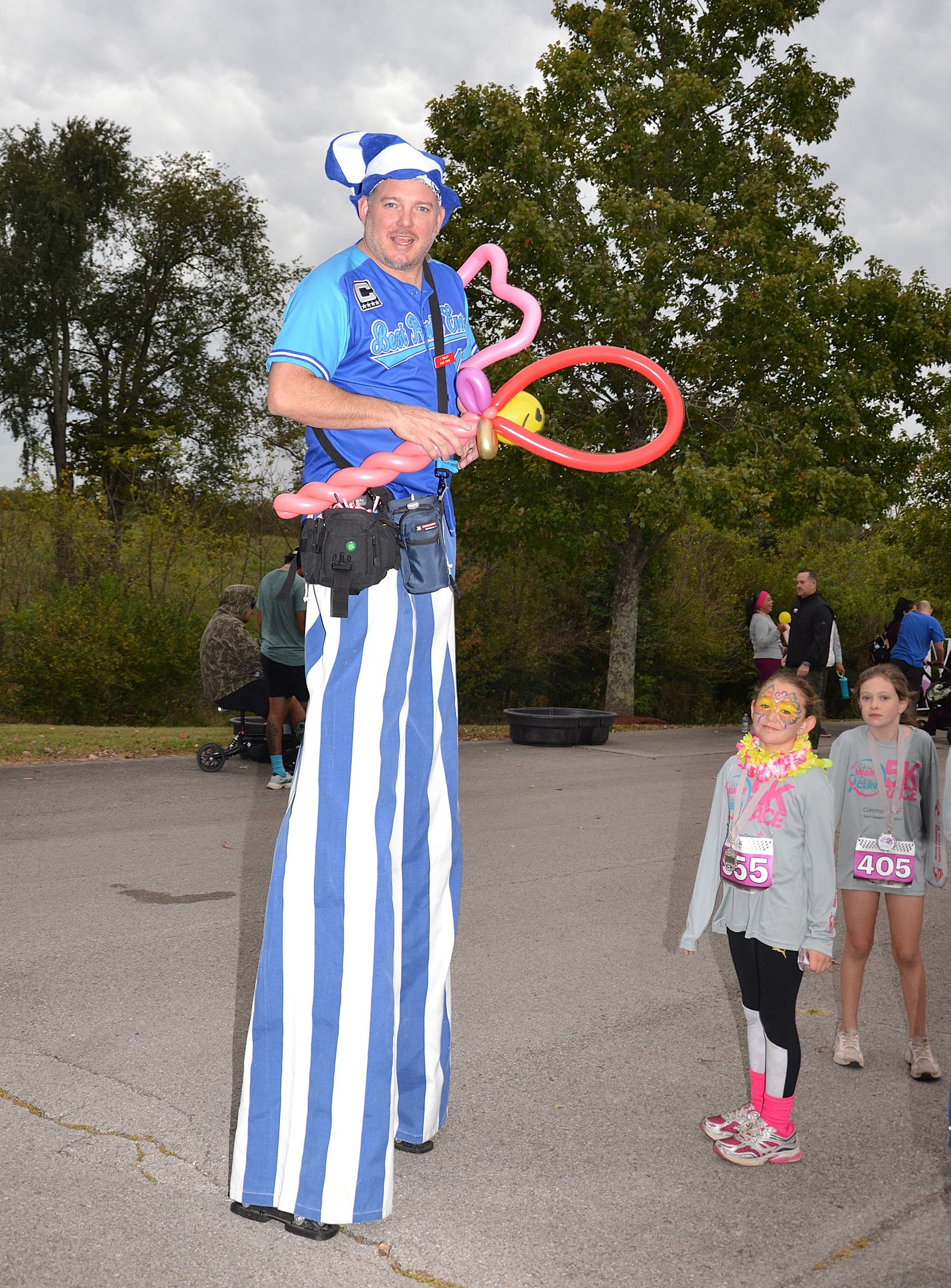 A stilt walker in blue and white stripes making balloon animals